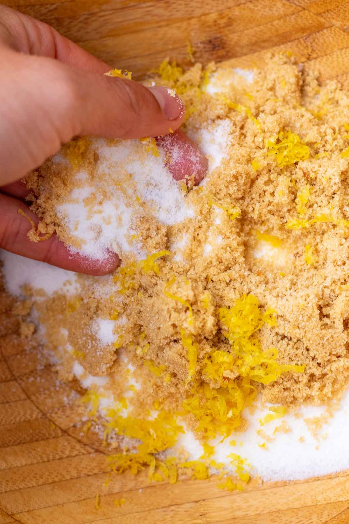 Hand rubbing lemon zest into bowl of sugar.