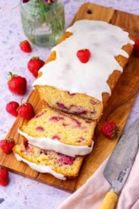Sliced sourdough strawberry bread on a cutting board surrounded by strawberries.