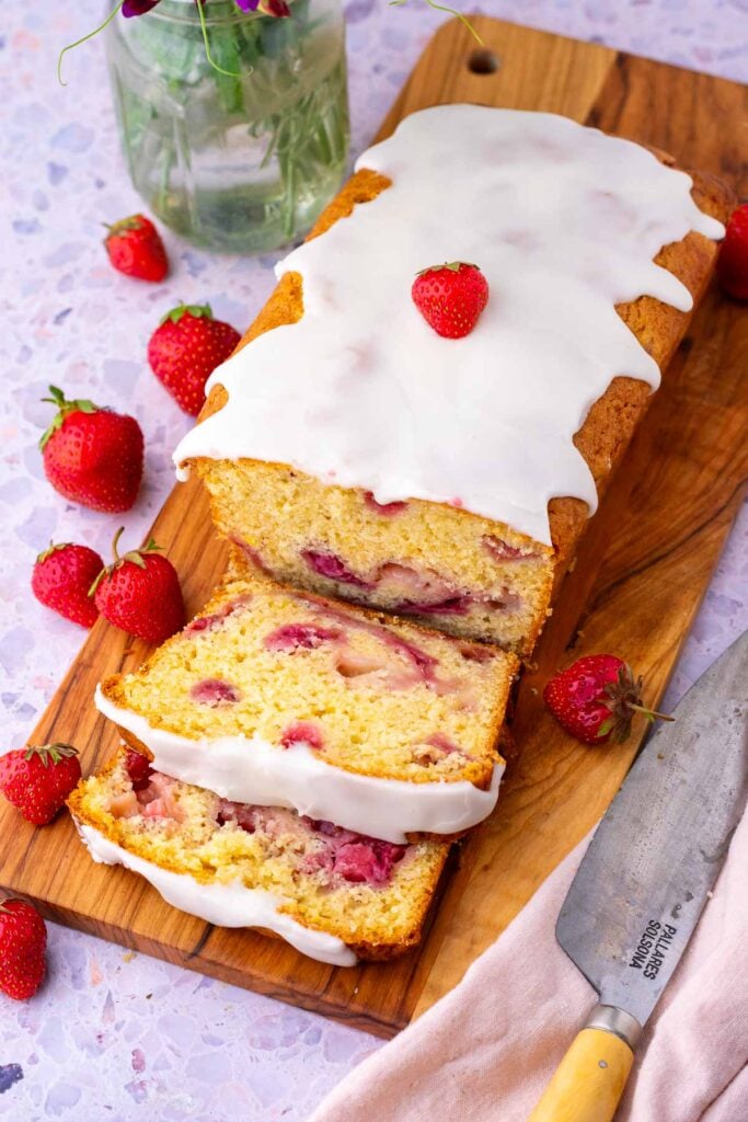 Sliced sourdough strawberry bread on a cutting board surrounded by strawberries.