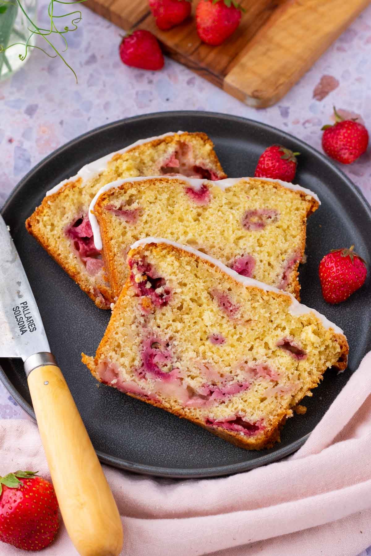 Slices of Sourdough Strawberry Bread on a plate surrounded by strawberries and a knife.