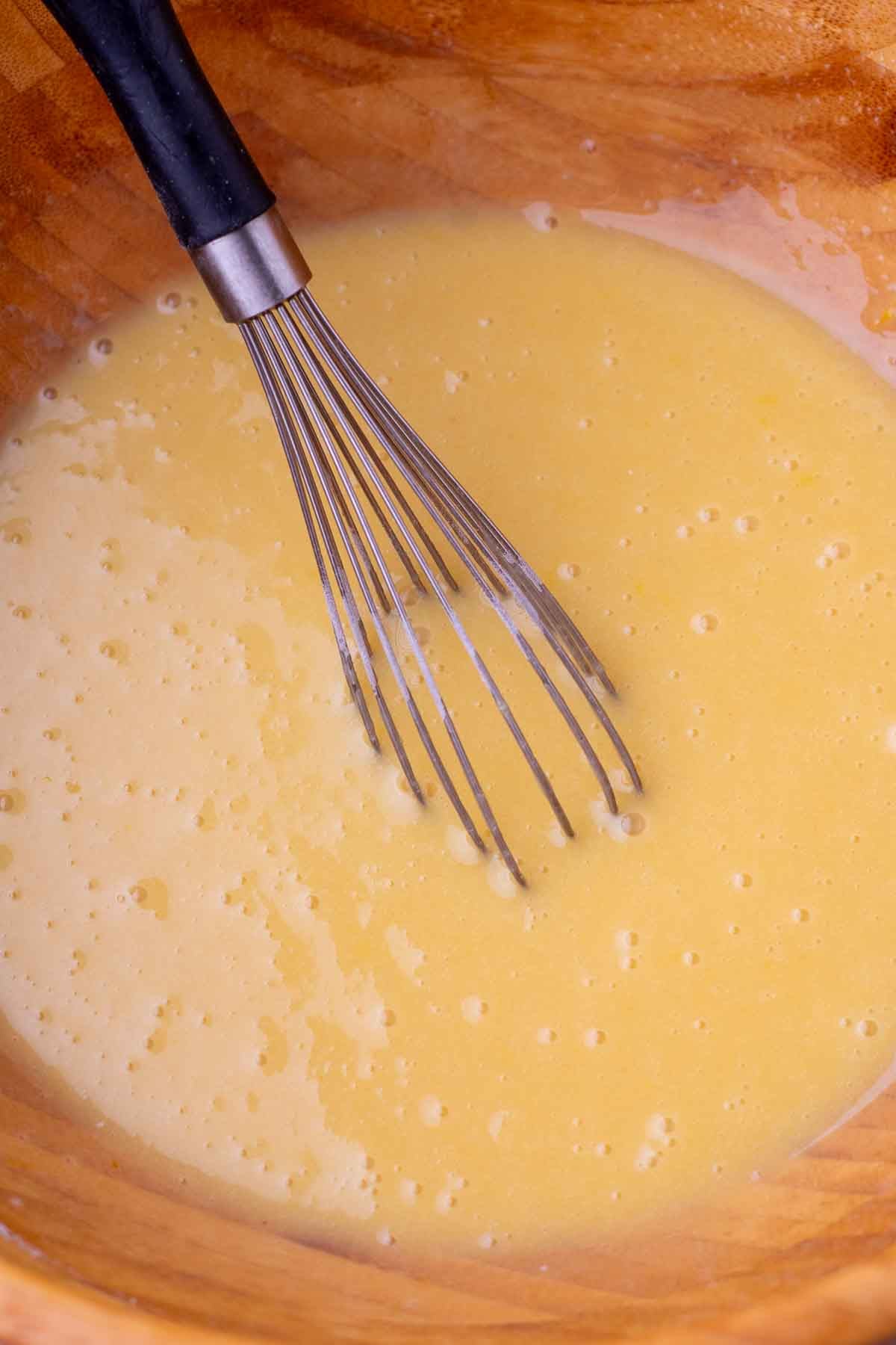 Mixed wet ingredients for Sourdough Strawberry Bread in a bowl with a whisk.