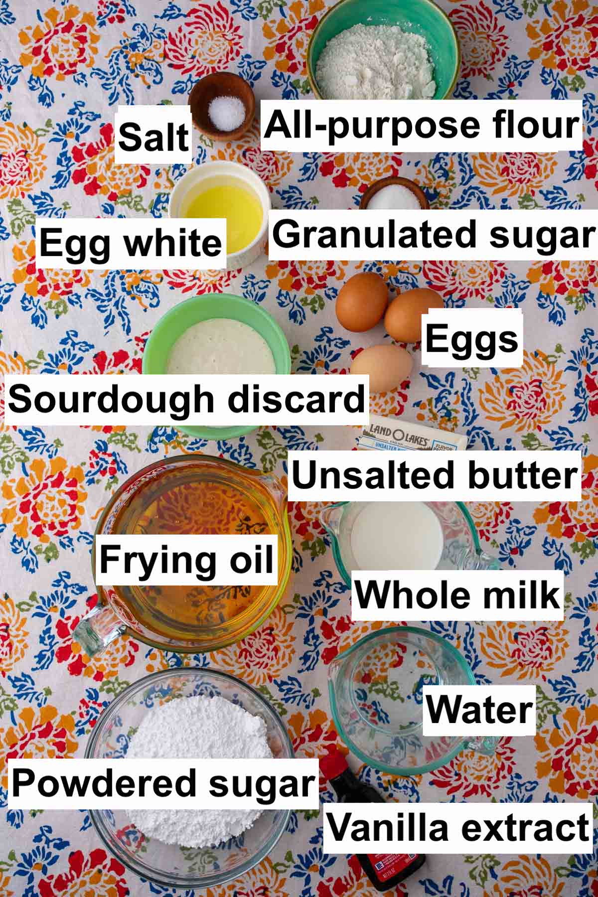 Labeled bowls of ingredients needed for sourdough crullers including all-purpose flour, salt, egg white, granulated sugar, eggs, sourdough discard, unsalted butter, frying oil, whole milk, water, powdered sugar, and vanilla extract.