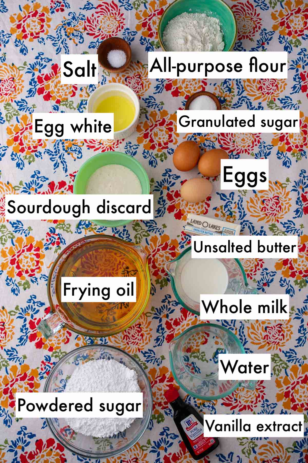 Labeled bowls of ingredients needed for sourdough crullers including all-purpose flour, salt, egg white, granulated sugar, eggs, sourdough discard, unsalted butter, frying oil, whole milk, water, powdered sugar, and vanilla extract.