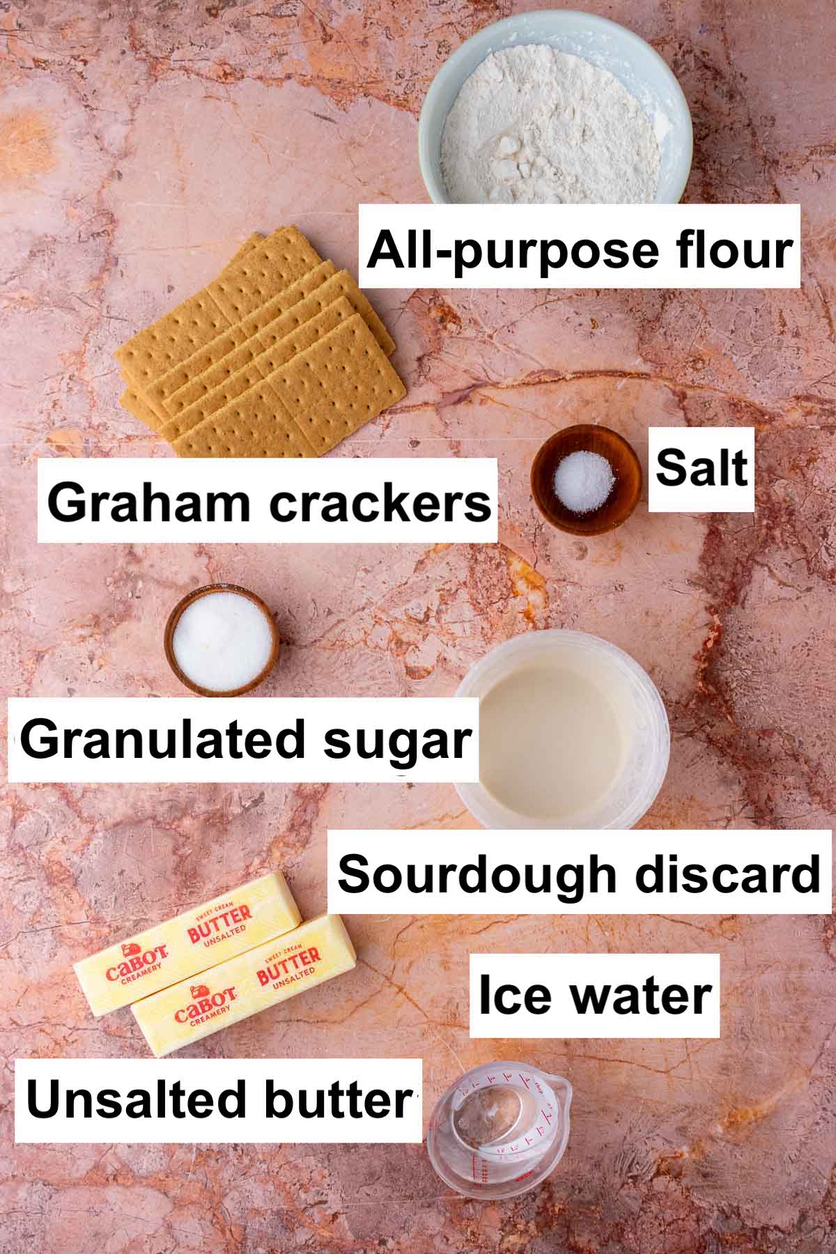 Labeled ingredients needed for sourdough graham cracker pie crust including all-purpose flour, graham crackers, salt, granulated sugar, sourdough discard, ice water, and unsalted butter.