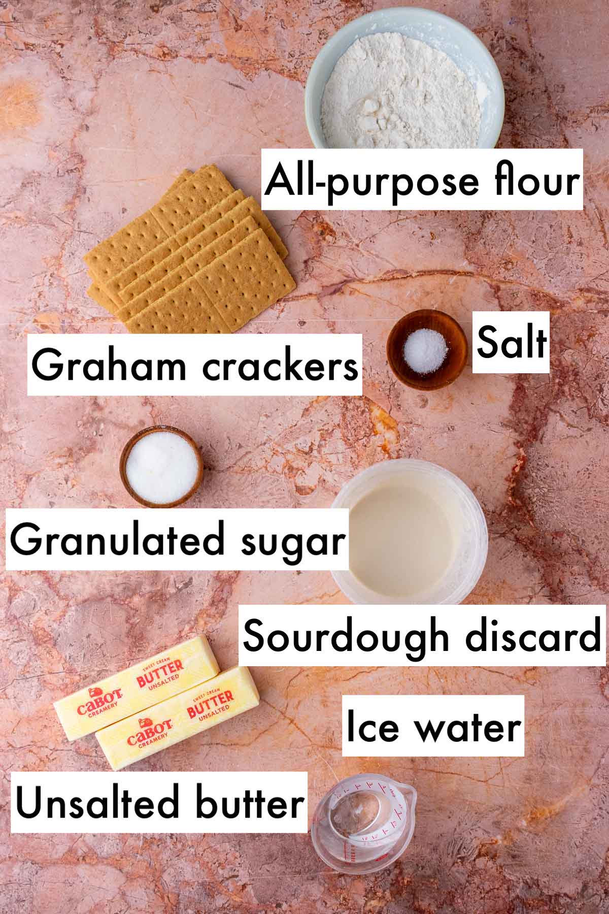 Labeled ingredients needed for sourdough graham cracker pie crust including all-purpose flour, graham crackers, salt, granulated sugar, sourdough discard, ice water, and unsalted butter.