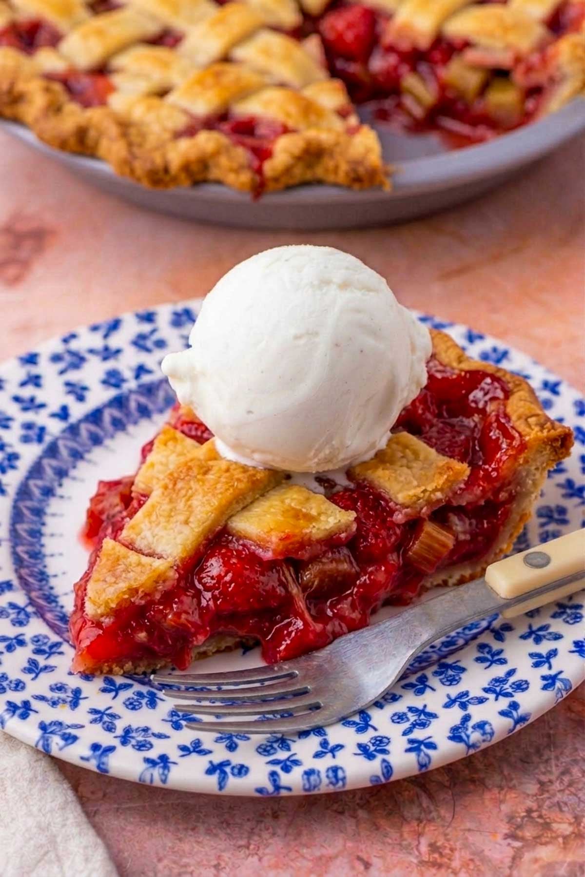 Slice of sourdough strawberry rhubarb pie with a scoop of vanilla ice cream on a plate with a fork.