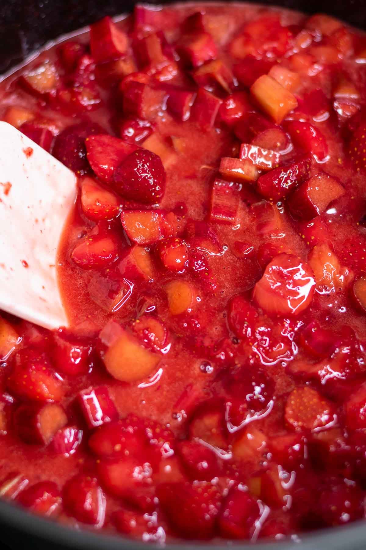 Cooking strawberry rhubarb pie filling on stovetop with a spatula.