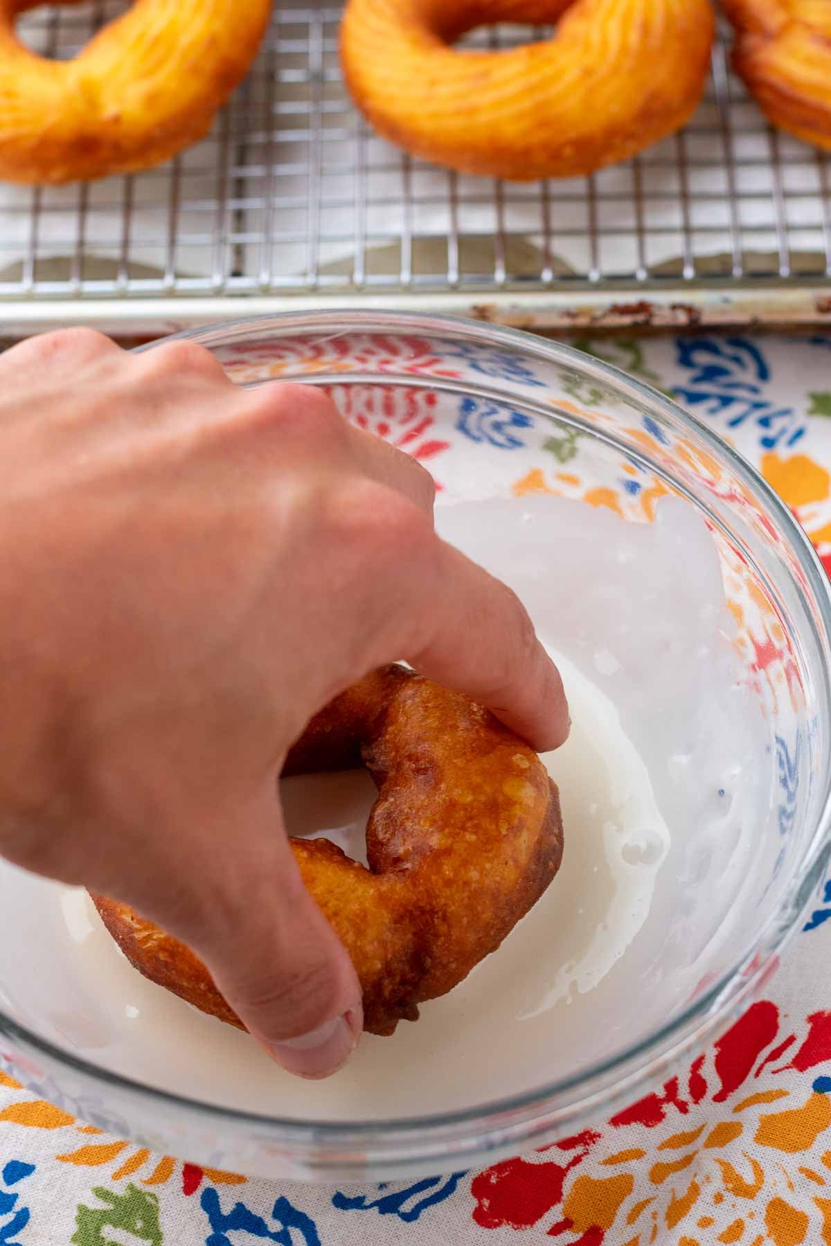Hand dipping a friend sourdough cruller into a bowl of glaze.