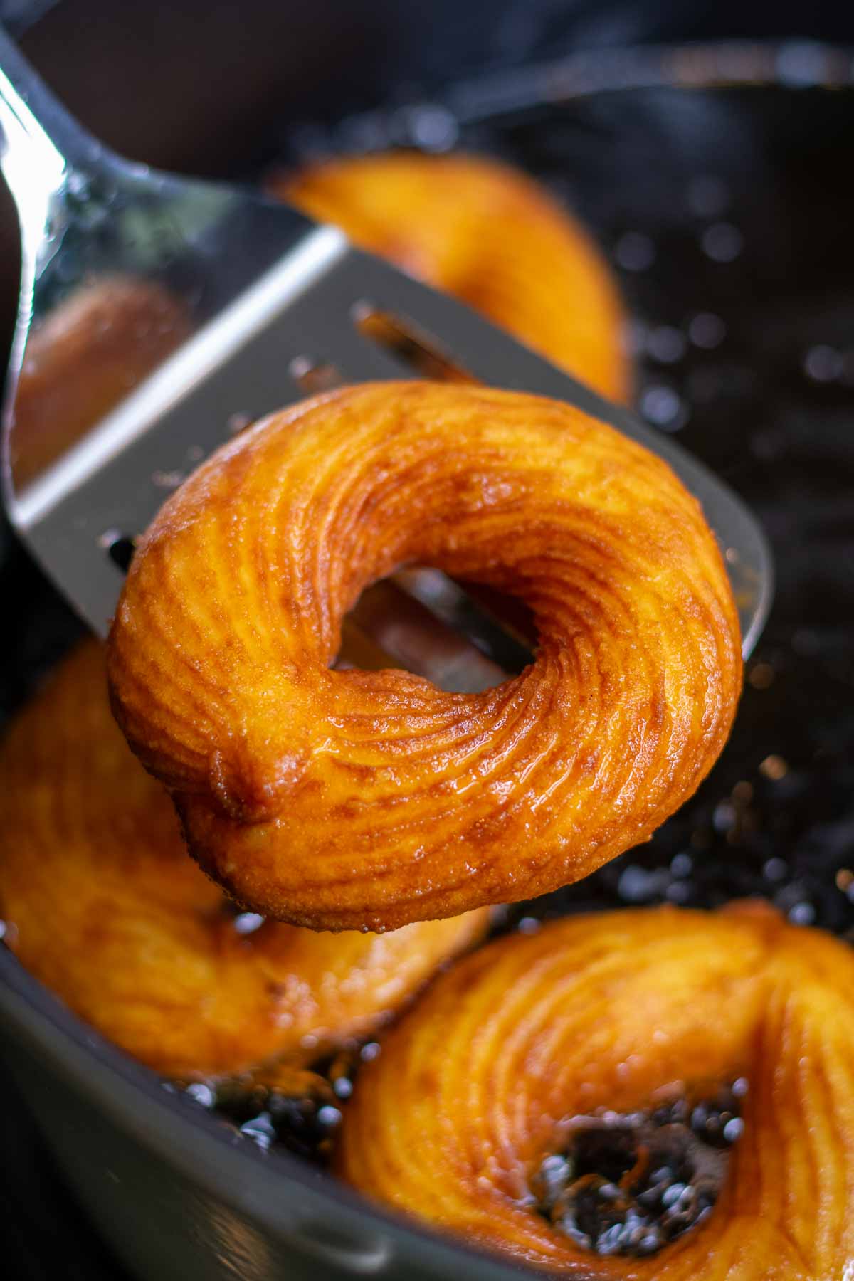 Spatula lifting a fried sourdough cruller over oil.