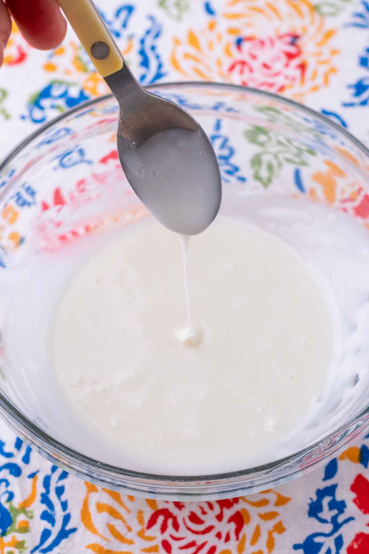 Spoon dripping glaze into a bowl of glaze for sourdough crullers.