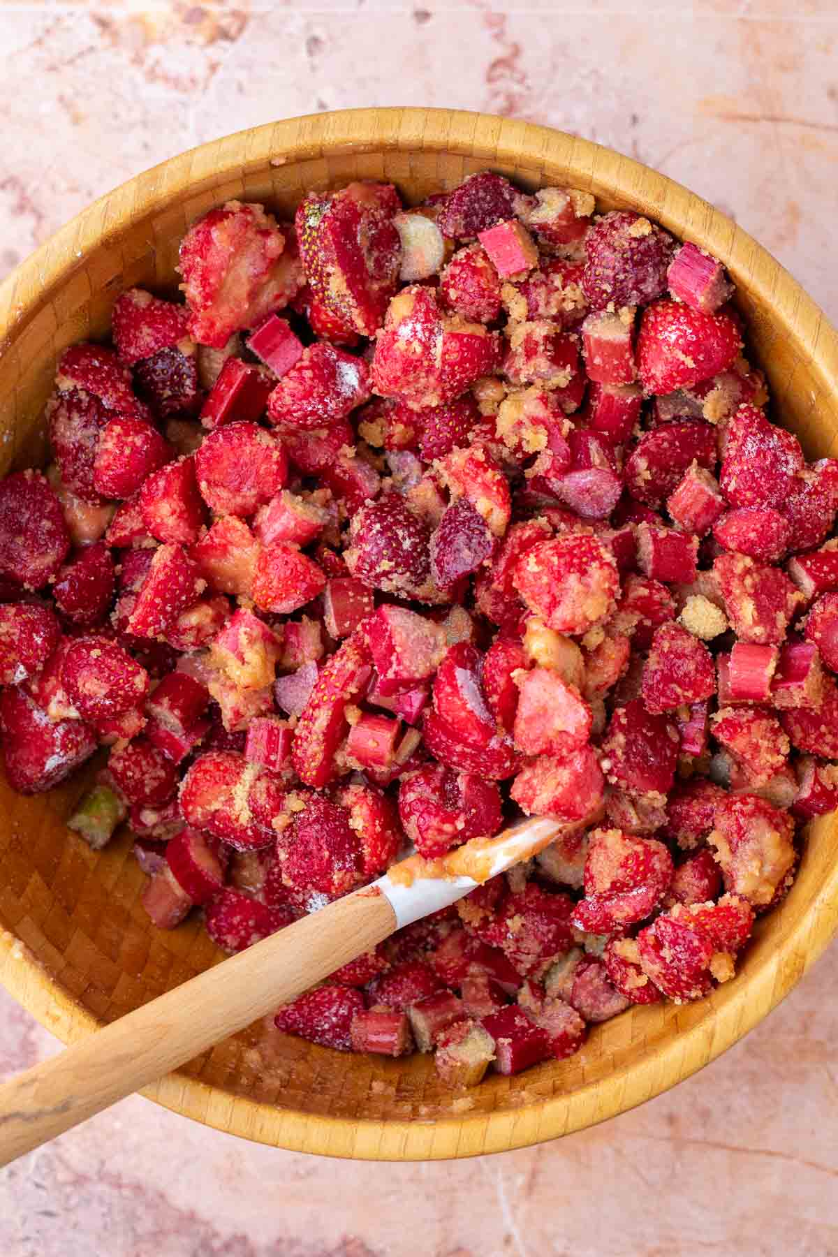 Stirring strawberry rhubarb pie filling in a large wooden bowl with a spatula.