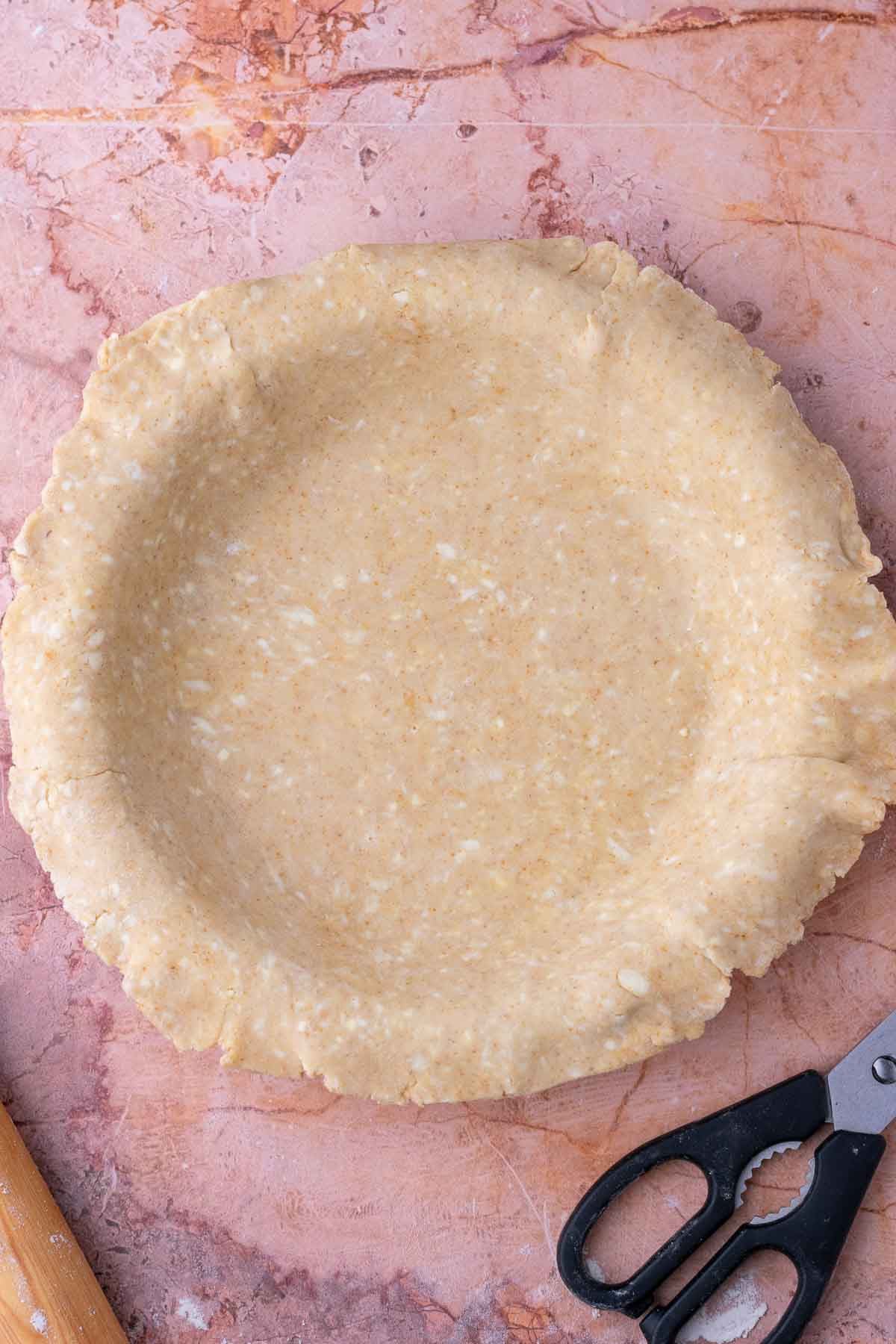 Sourdough graham cracker pie crust in a pie plate with a pair of pastry scissors.