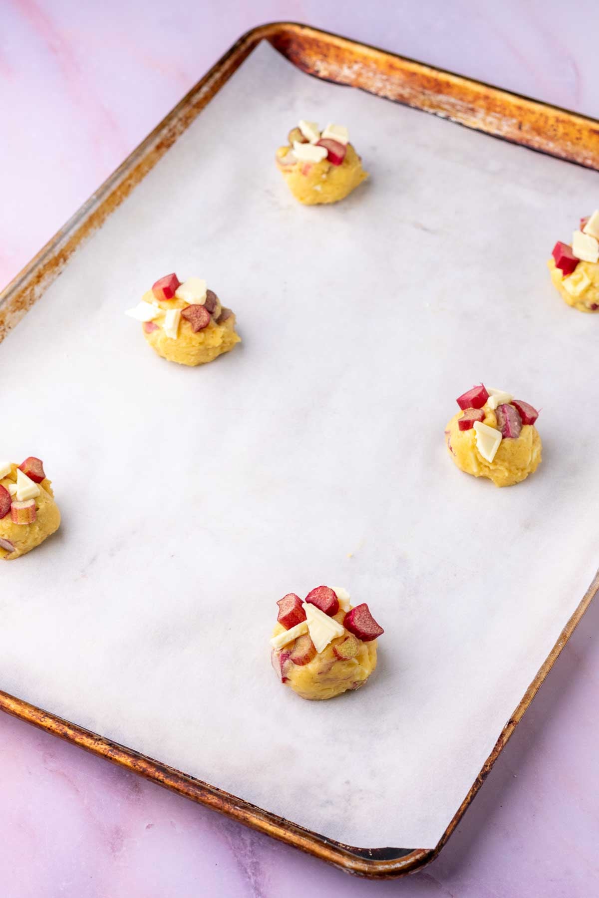 Sheet pan lined with parchment paper with six sourdough rhubarb cookie dough balls before baking.