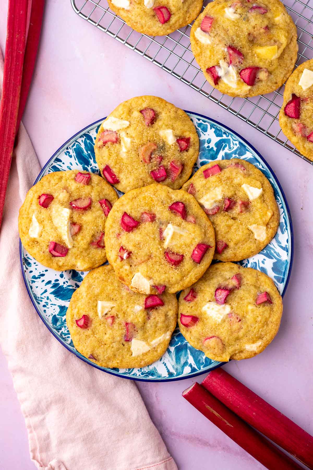 Blue and white enamel plate with sourdough rhubarb cookies surrounded by fresh rhubarb stalks.