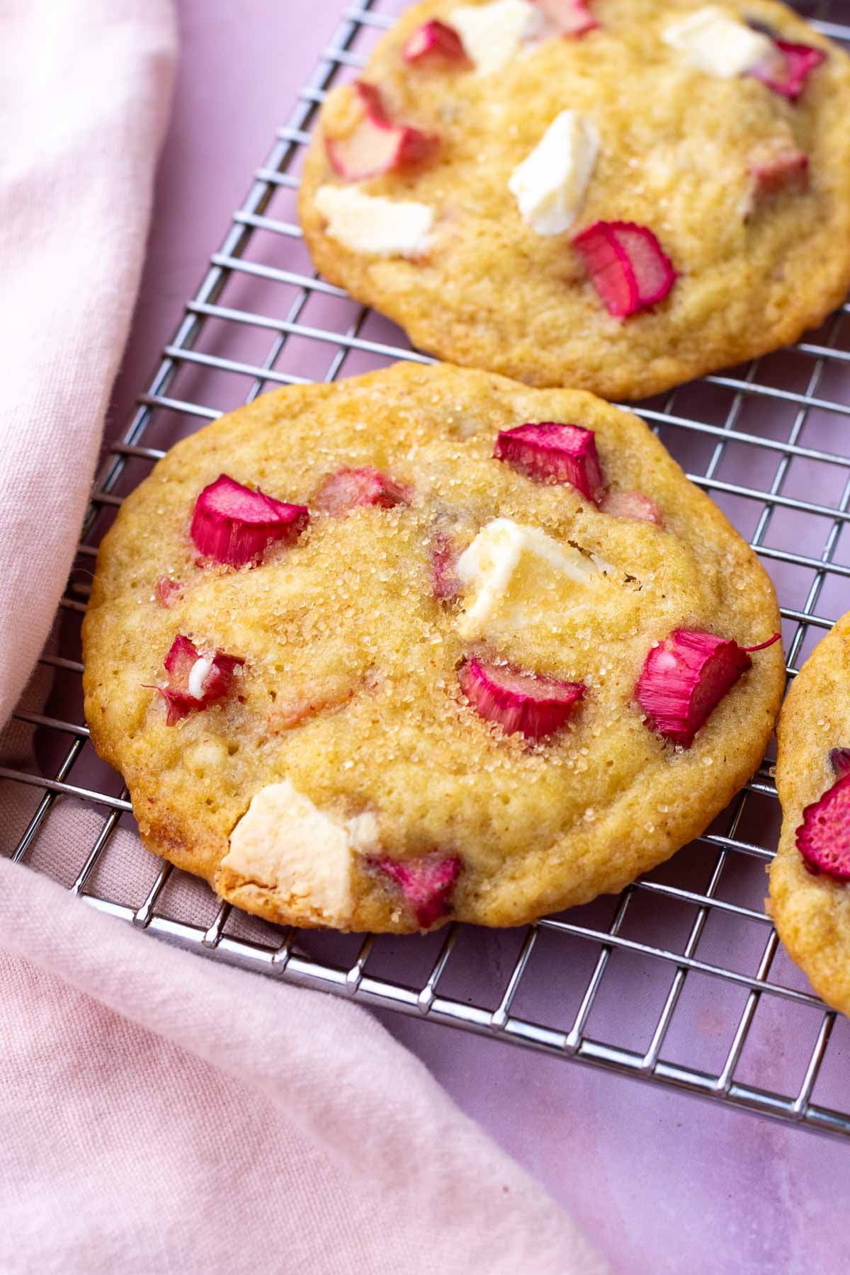 Wire rack with sourdough rhubarb cookies with white chocolate and a pink towel.