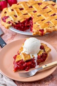Slice of sourdough strawberry rhubarb pie with a scoop of vanilla ice cream on a plate with a fork and the entire pie in the background.