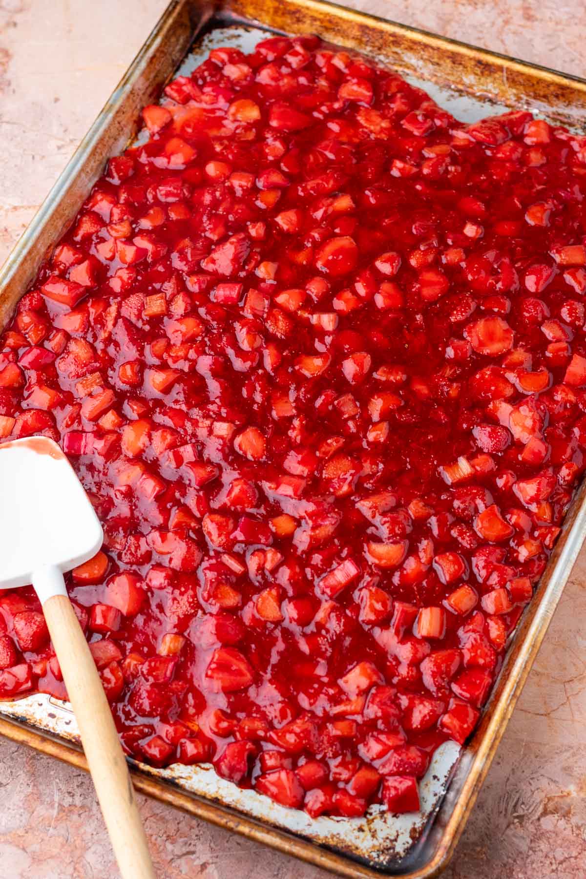 Strawberry rhubarb pie filling cooling on a large sheet pan with a spatula.