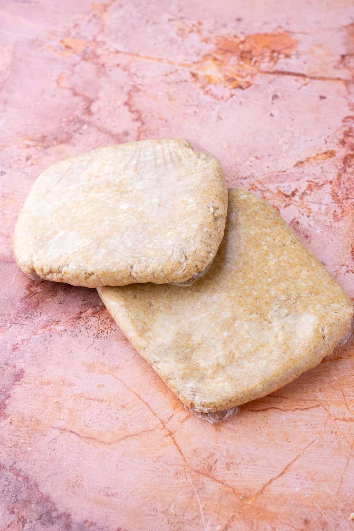 Two sourdough graham cracker pie crust discs wrapped in plastic wrap.
