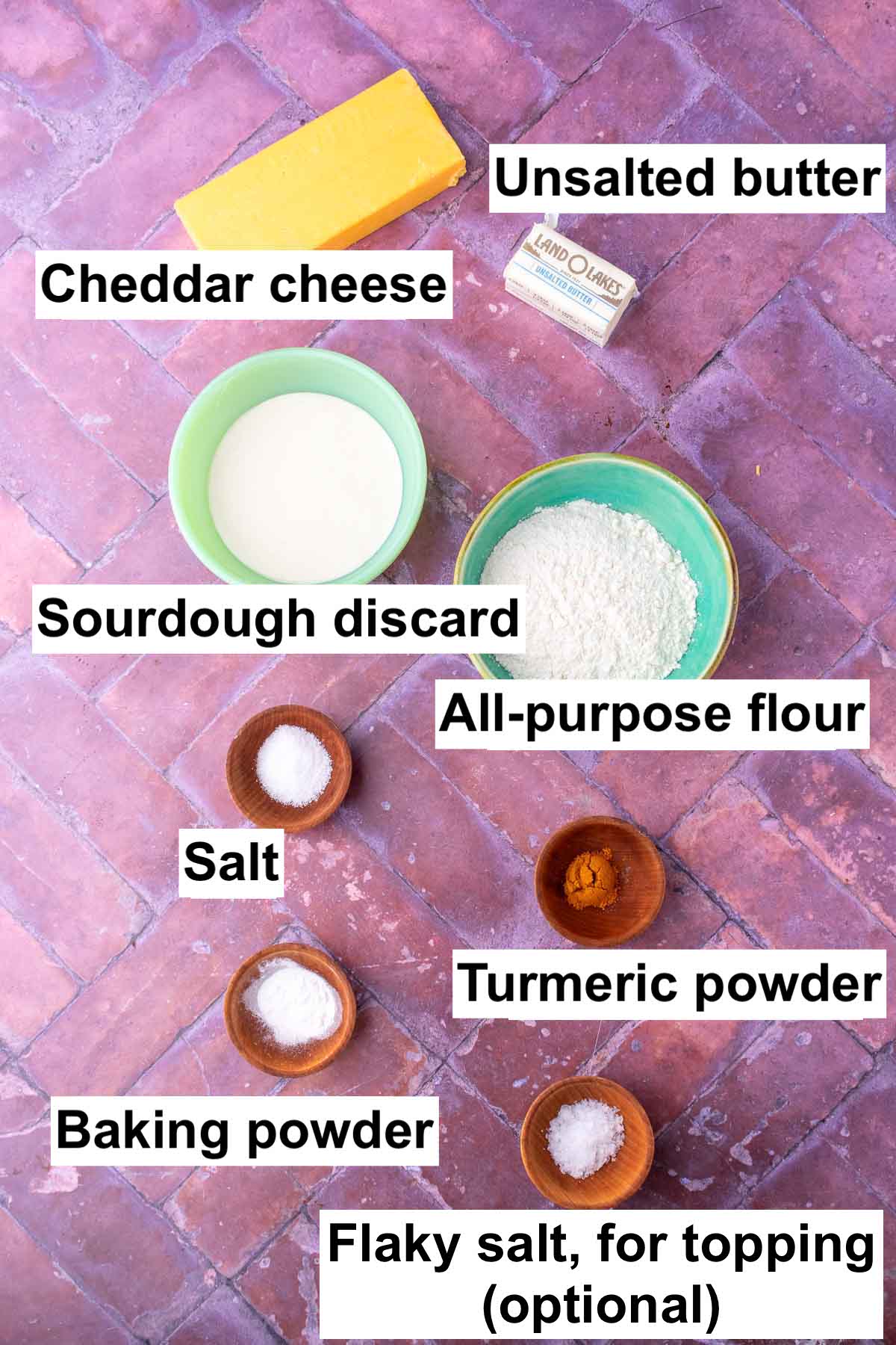 Labeled bowls of ingredients needed for sourdough goldfish including cheddar cheese, unsalted butter, sourdough discard, all-purpose flour, salt, turmeric, baking powder, and flaky salt.