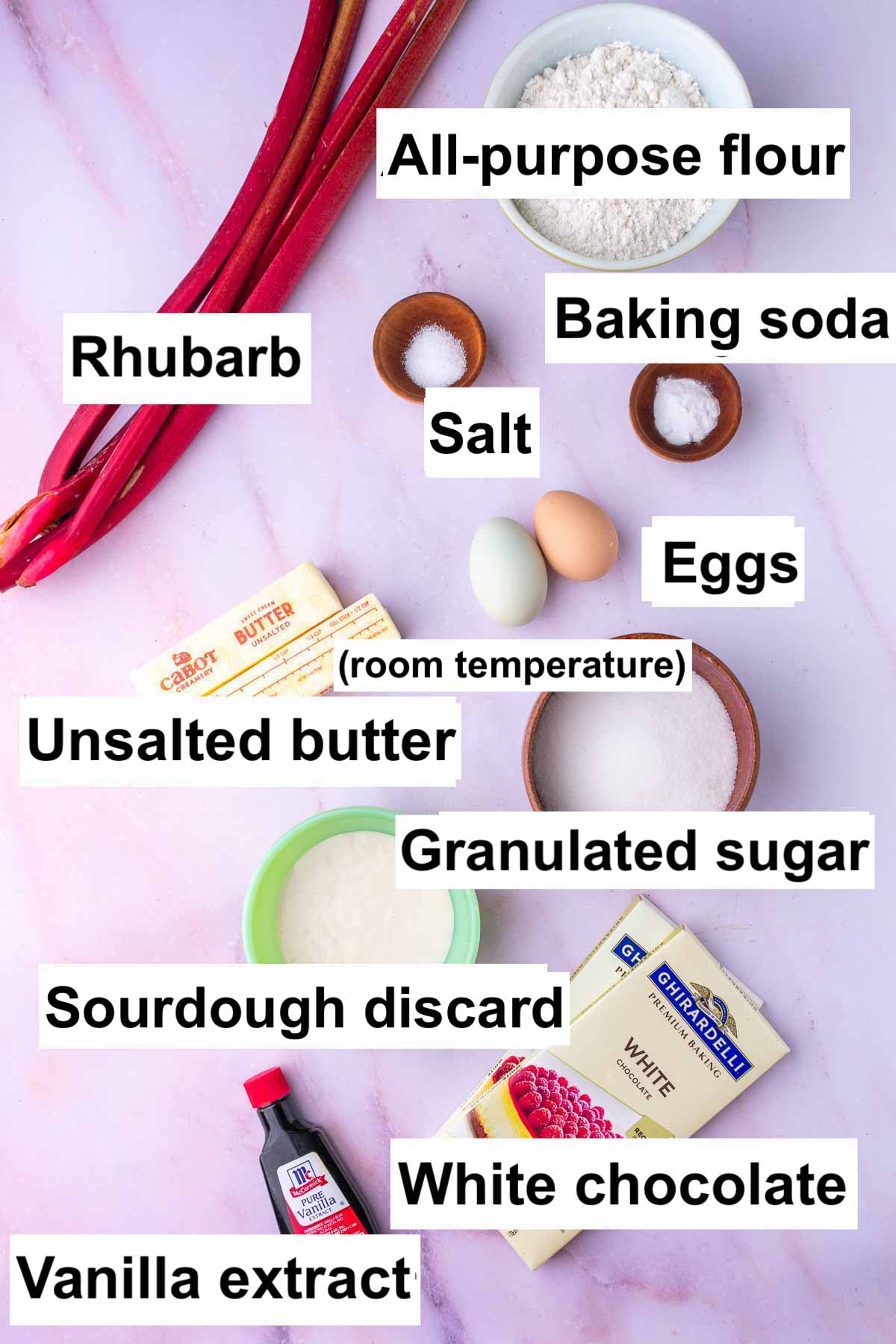 Labeled ingredients needed for sourdough rhubarb cookies including all-purpose flour, baking soda, rhubarb, salt, eggs, unsalted butter, granulated sugar, sourdough discard, white chocolate, and vanilla extract.