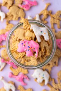 Close up of sourdough animal crackers in a jar with some frosted with pink and white frosting and sprinkles.