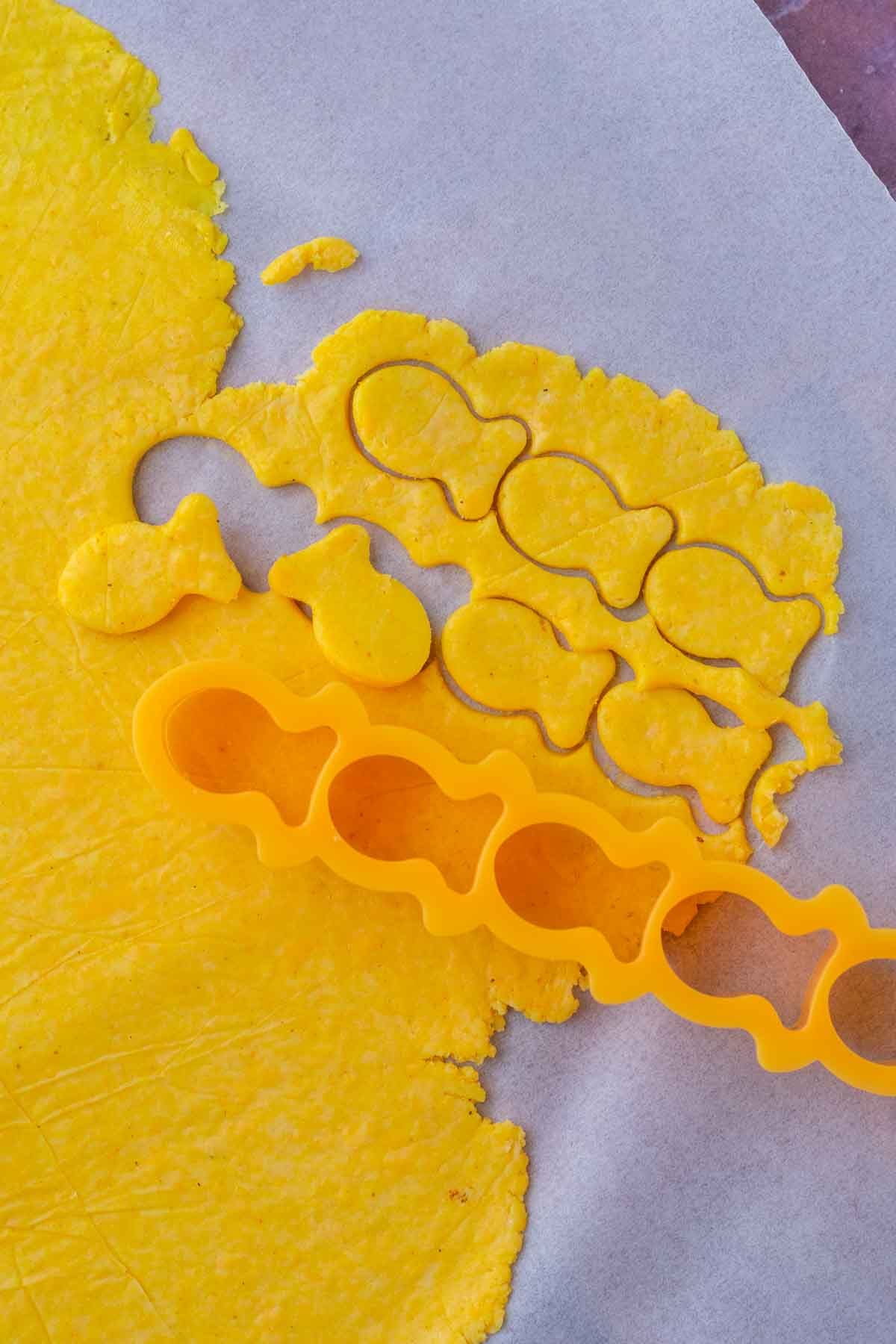 Cutting out sourdough goldfish with a fish cutter on parchment paper.
