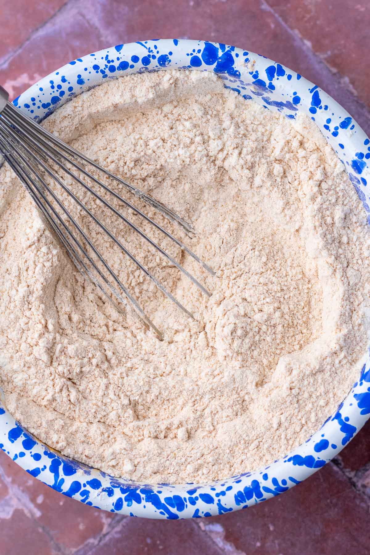 Whisk mixing dry ingredients for sourdough teddy grahams in a blue and white splatter enamelware bowl.