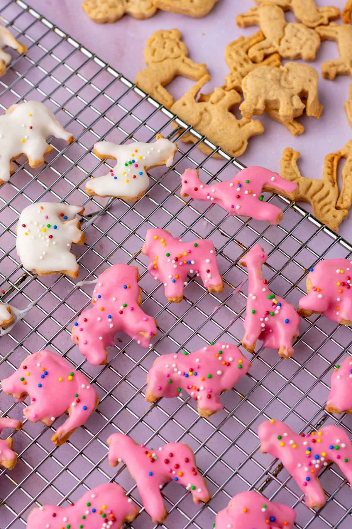Glazing sourdough animal crackers with pink and white frosting and sprinkles on a wire rack.