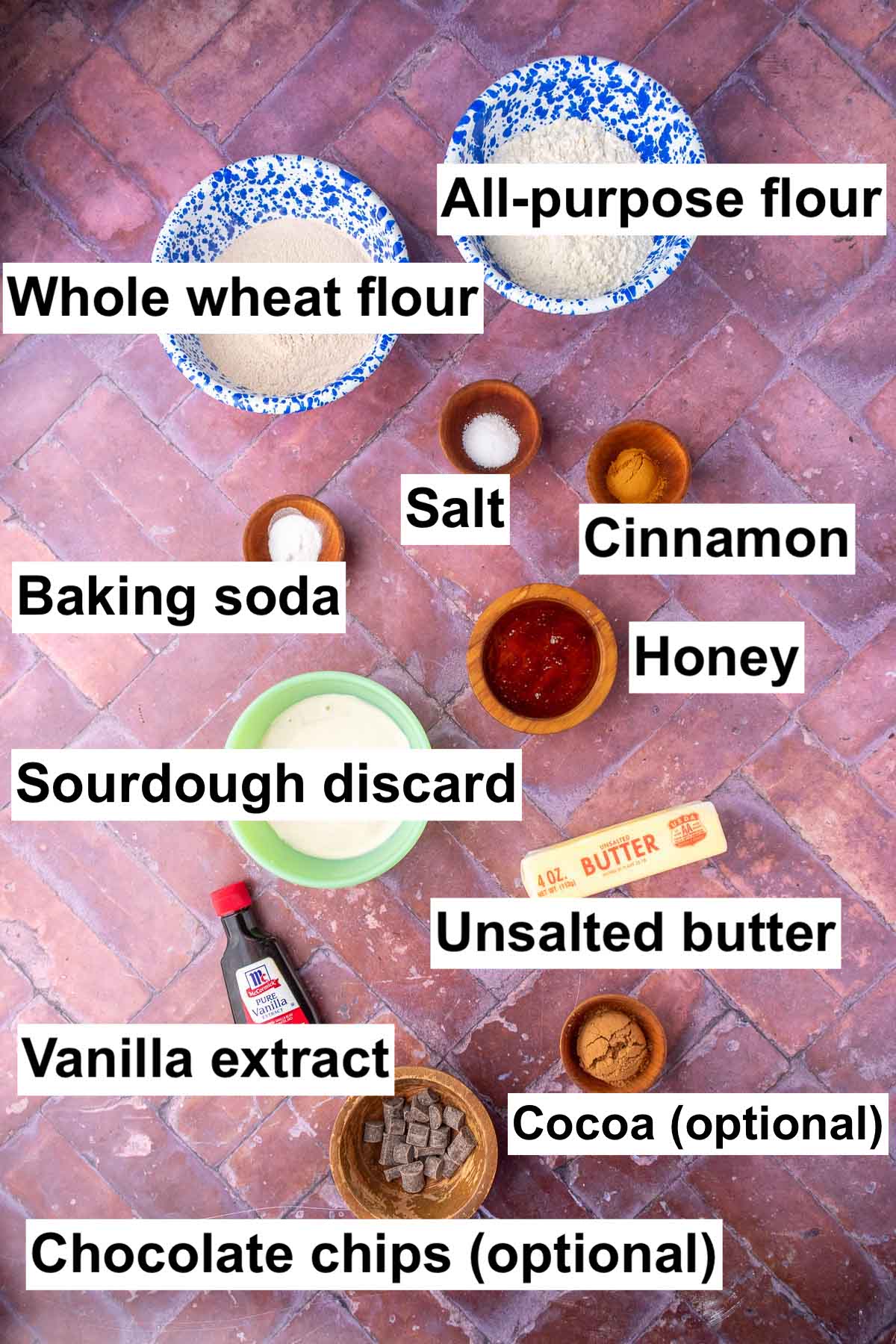 Bowls of ingredients needed for sourdough teddy grahams including all-purpose flour, whole wheat flour, salt, cinnamon, honey, baking soda, sourdough discard, unsalted butter, vanilla, cocoa, and chocolate chips.