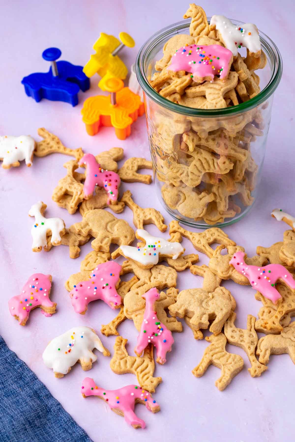 sourdough animal crackers, some frosted with sprinkles, in a glass jar and some scattered around with animal cookie cutters.