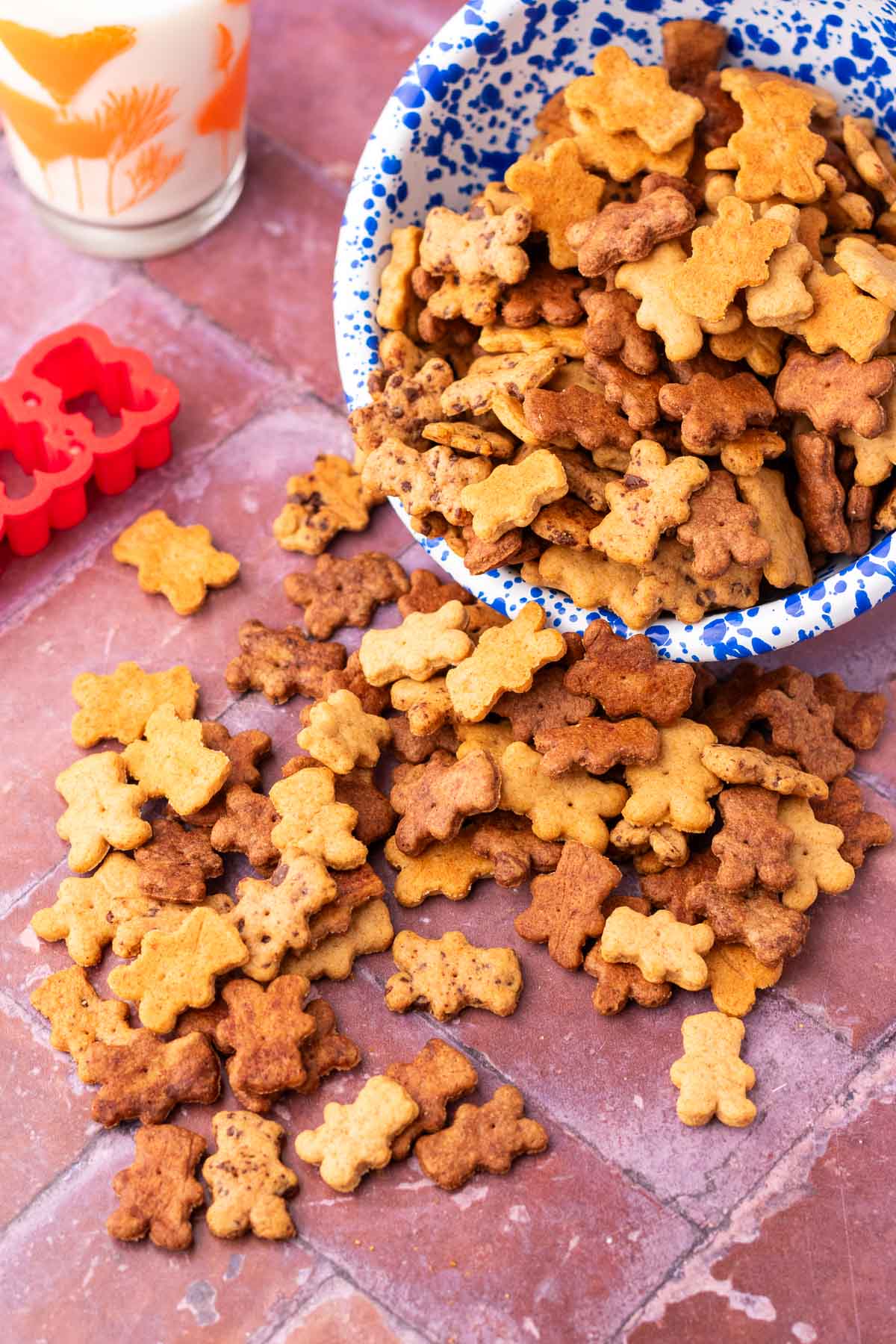 Sourdough teddy grahams pouring out of a blue and white enamelware bowl with a glass of milk in the background.