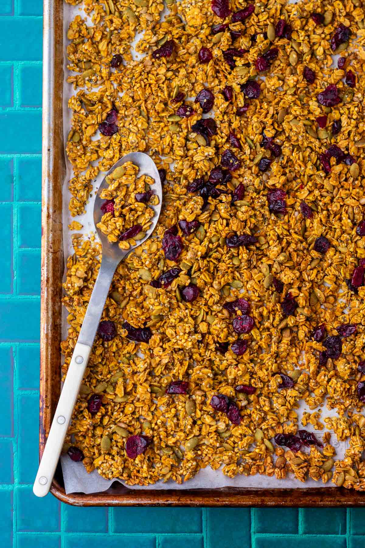Baked sourdough pumpkin granola in a sheet pan with a large spoon.