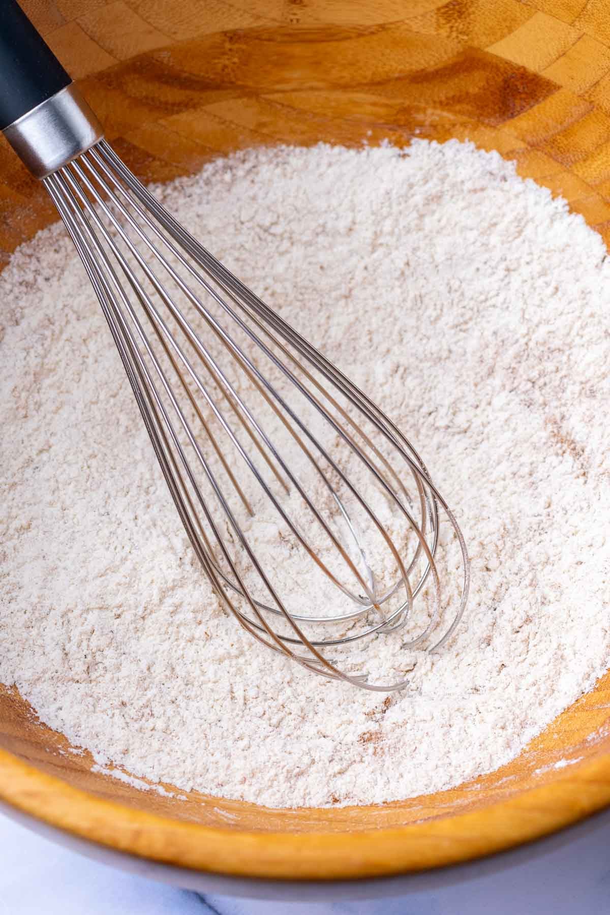 Whisk in a wooden bowl with dry ingredients for sourdough pumpkin cupcakes.