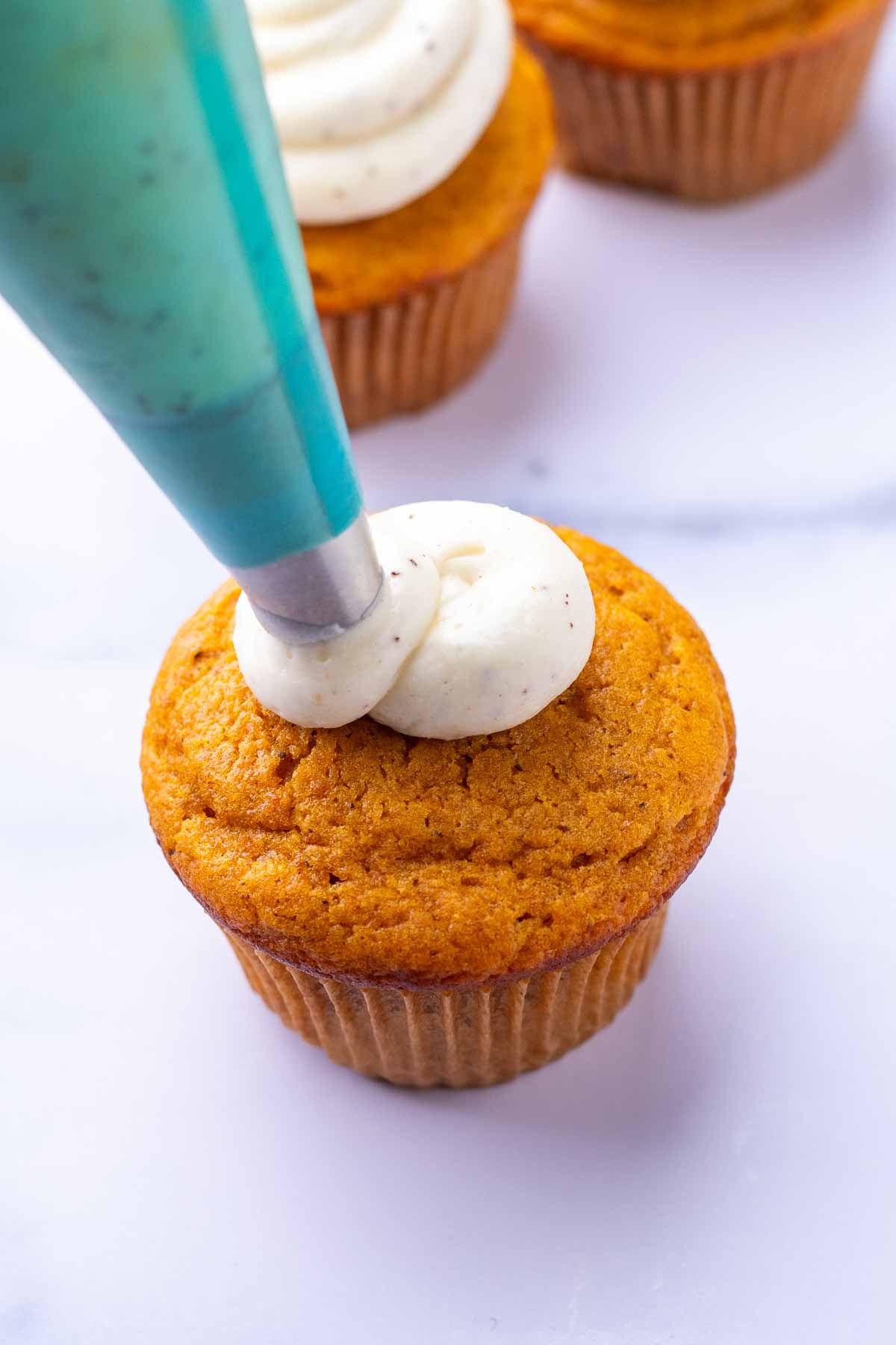 Piping brown butter cream cheese frosting on a sourdough pumpkin cupcake.