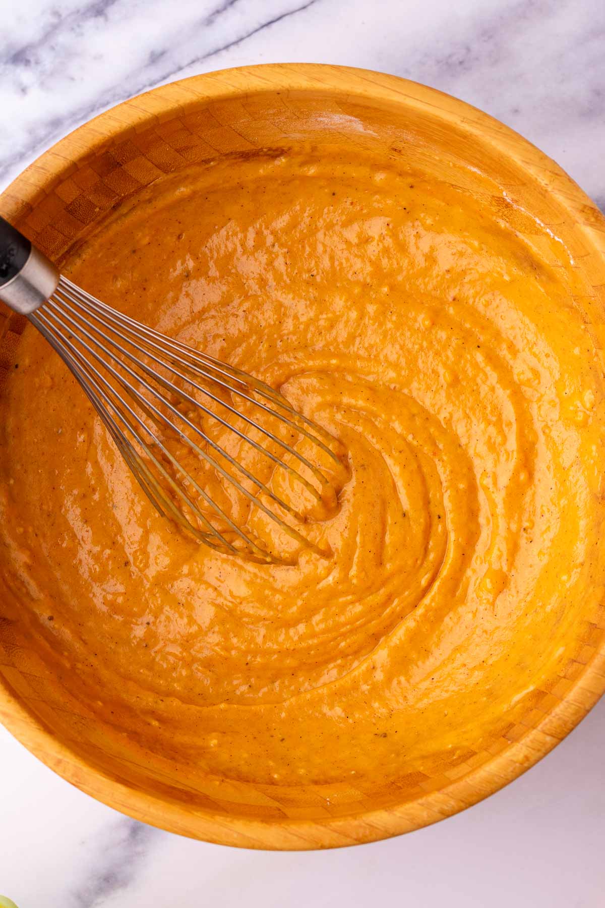 Whisk mixing sourdough pumpkin cupcake batter in a wooden bowl.