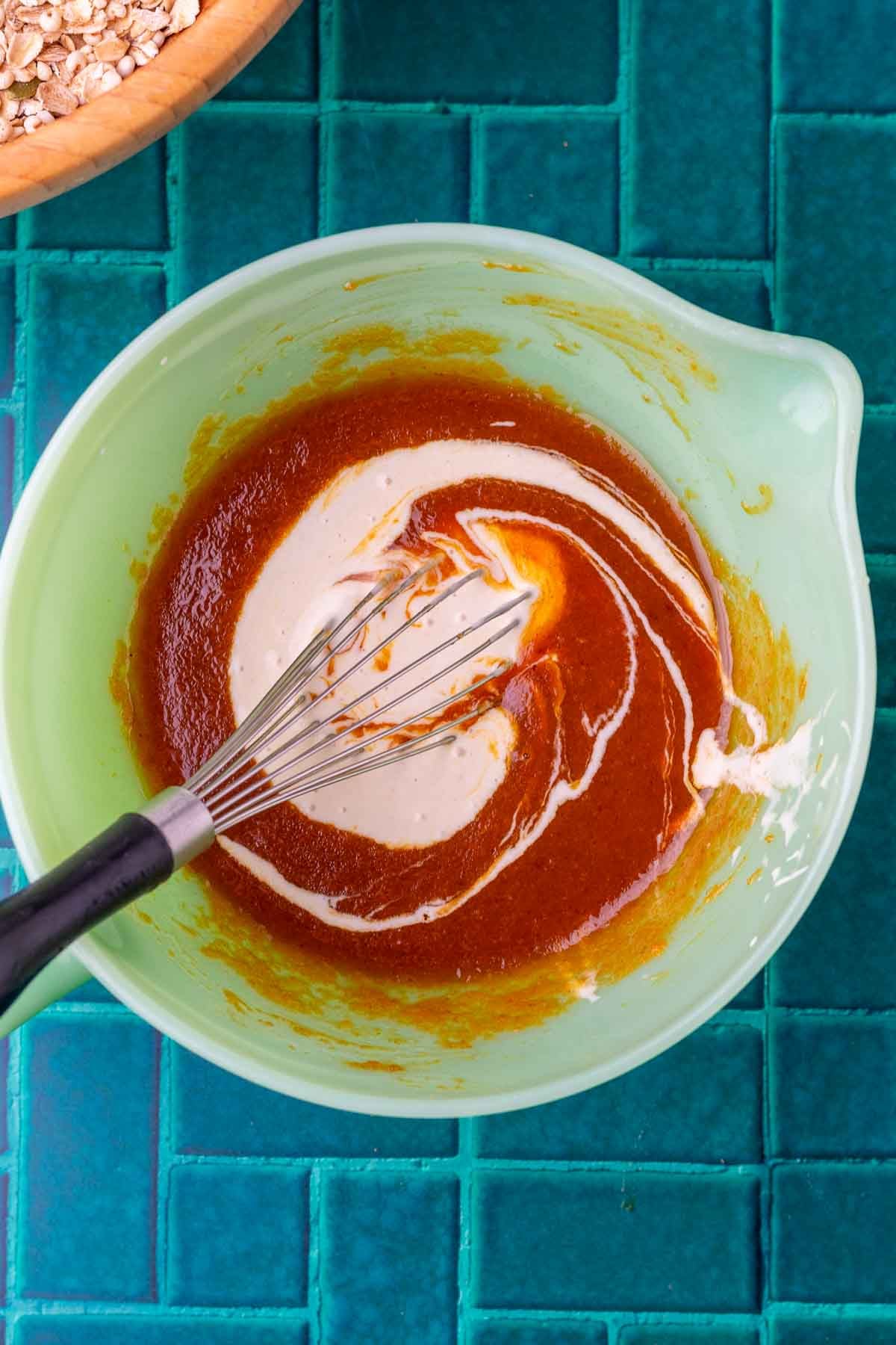 Whisk mixing the wet ingredients for sourdough pumpkin granola in a pourable mixing bowl.