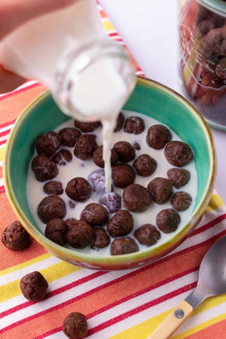 Pouring milk from a glass into a cereal bowl of sourdough cocoa puffs.