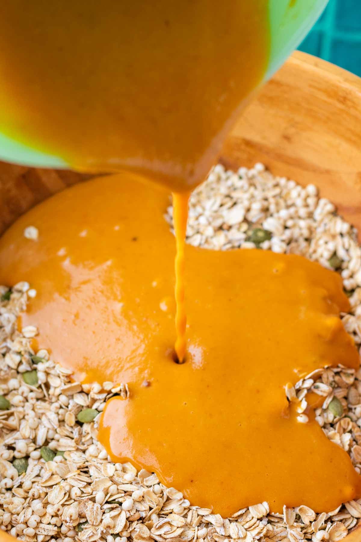 Pouring sourdough pumpkin granola wet ingredients into a bowl of dry ingredients including oats and seeds.