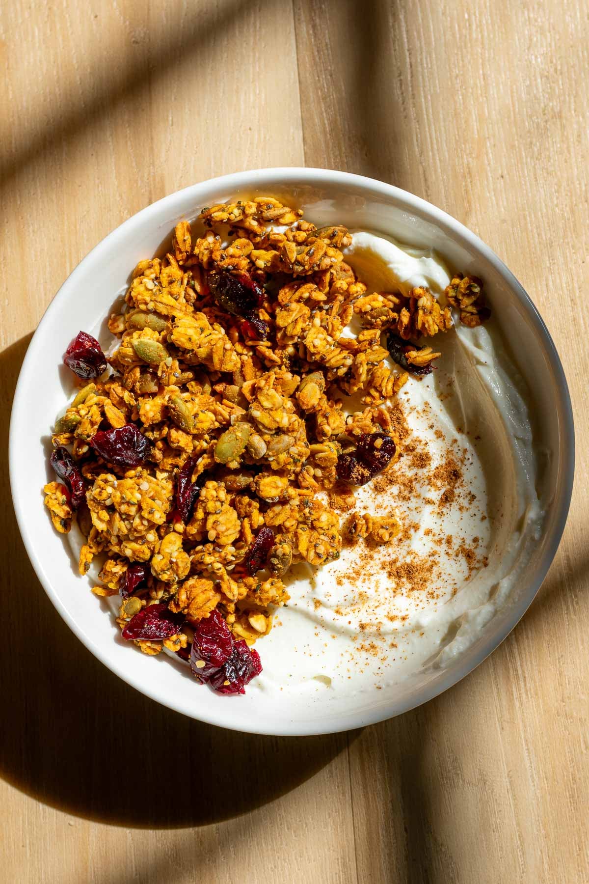 Bowl of sourdough pumpkin granola with dried cranberries in yogurt.
