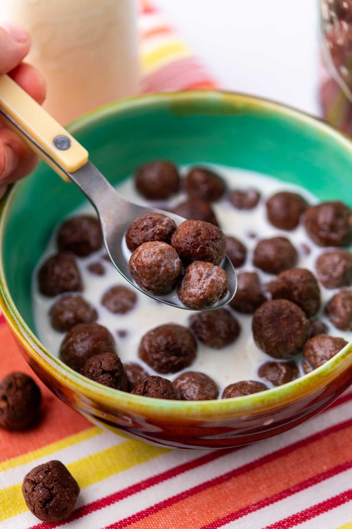 Spoon holding four sourdough cocoa puffs over a bowl of cereal with milk.