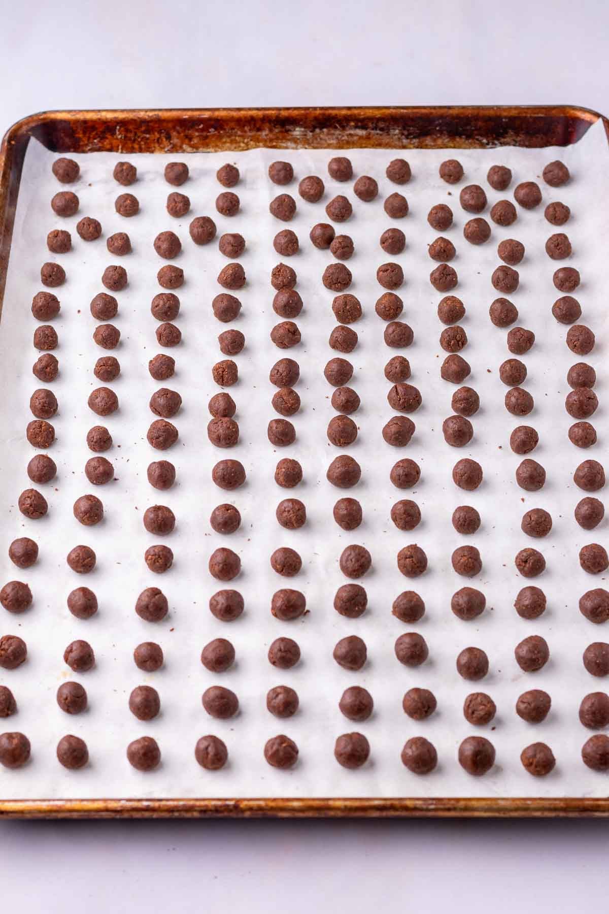 Unbaked sourdough cocoa puffs rolled into balls on a large sheet pan lined with parchment paper.