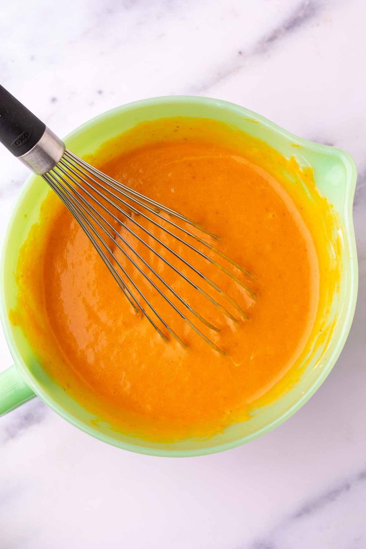 Whisk in a green mixing bowl mixing wet ingredients for sourdough pumpkin cupcakes.