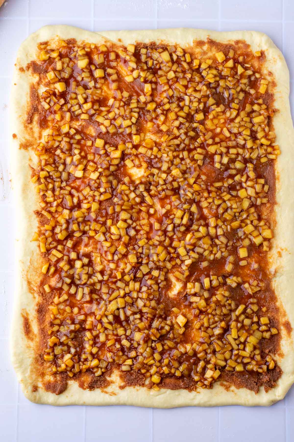 Rolled out dough in a rectangle with cinnamon sugar and apple pie filling.