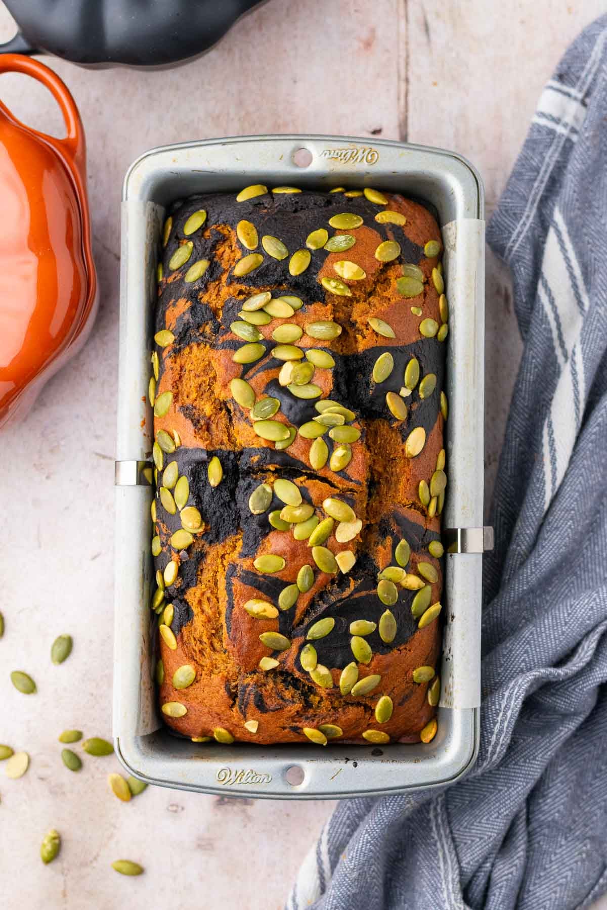 Baked sourdough pumpkin marble bread with pumpkin seeds on top in a loaf pan.