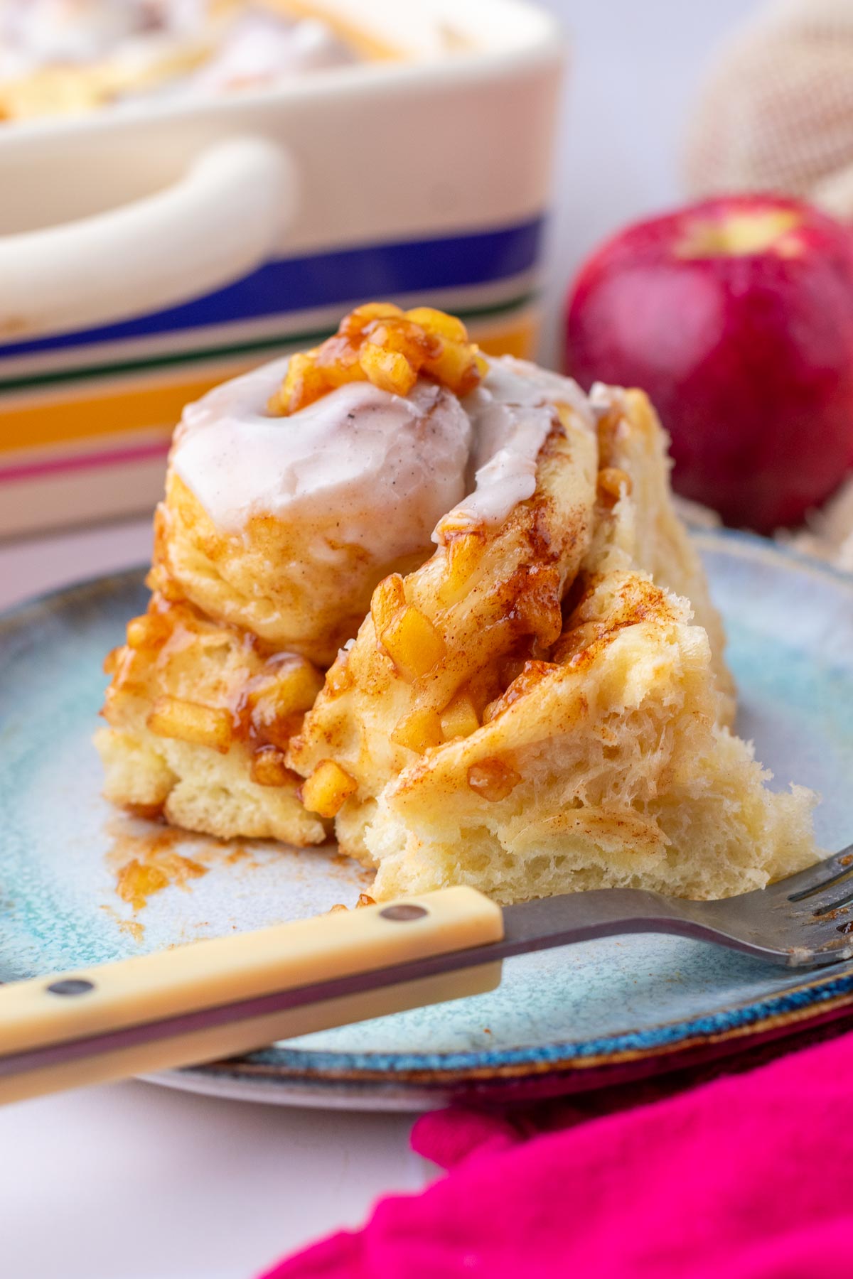 Close up of a sourdough apple cinnamon roll on a plate with vanilla icing.