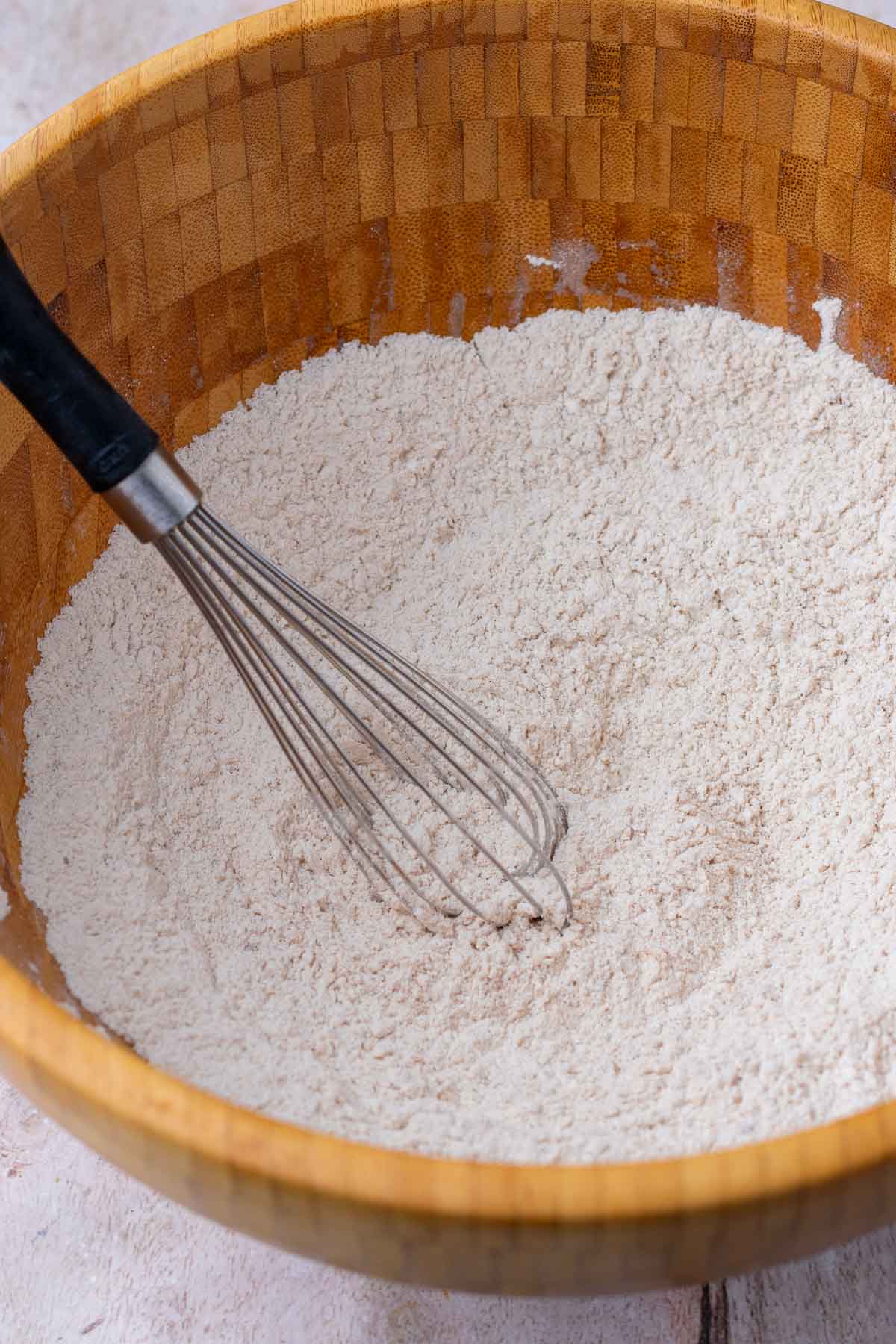 Whisking dry ingredients in a large wooden bowl with a whisk.