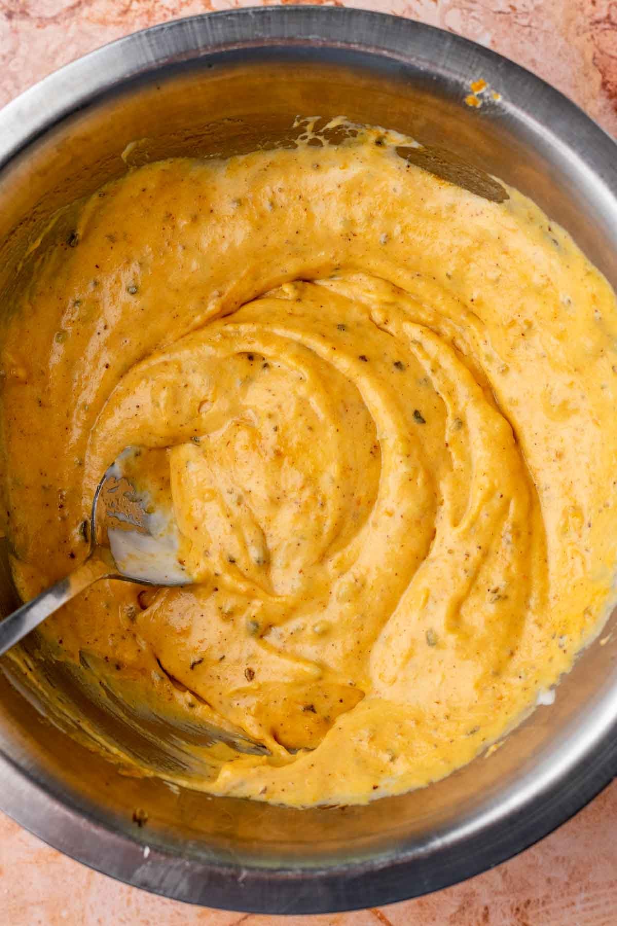 Bowl of mixed wet ingredients for sourdough pumpkin crackers with a spoon.