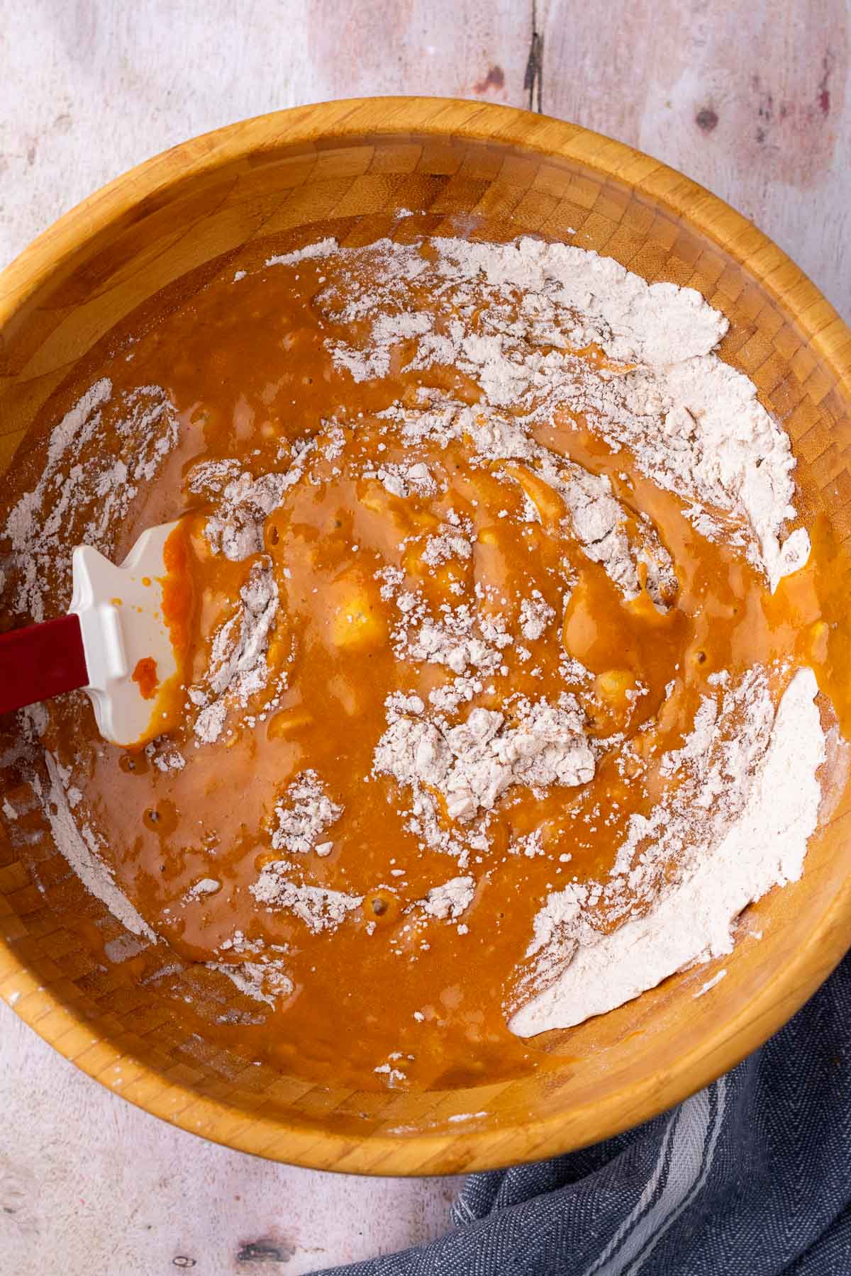 Mixing wet and dry ingredients for sourdough pumpkin marble bread in large wooden bowl with a spatula.