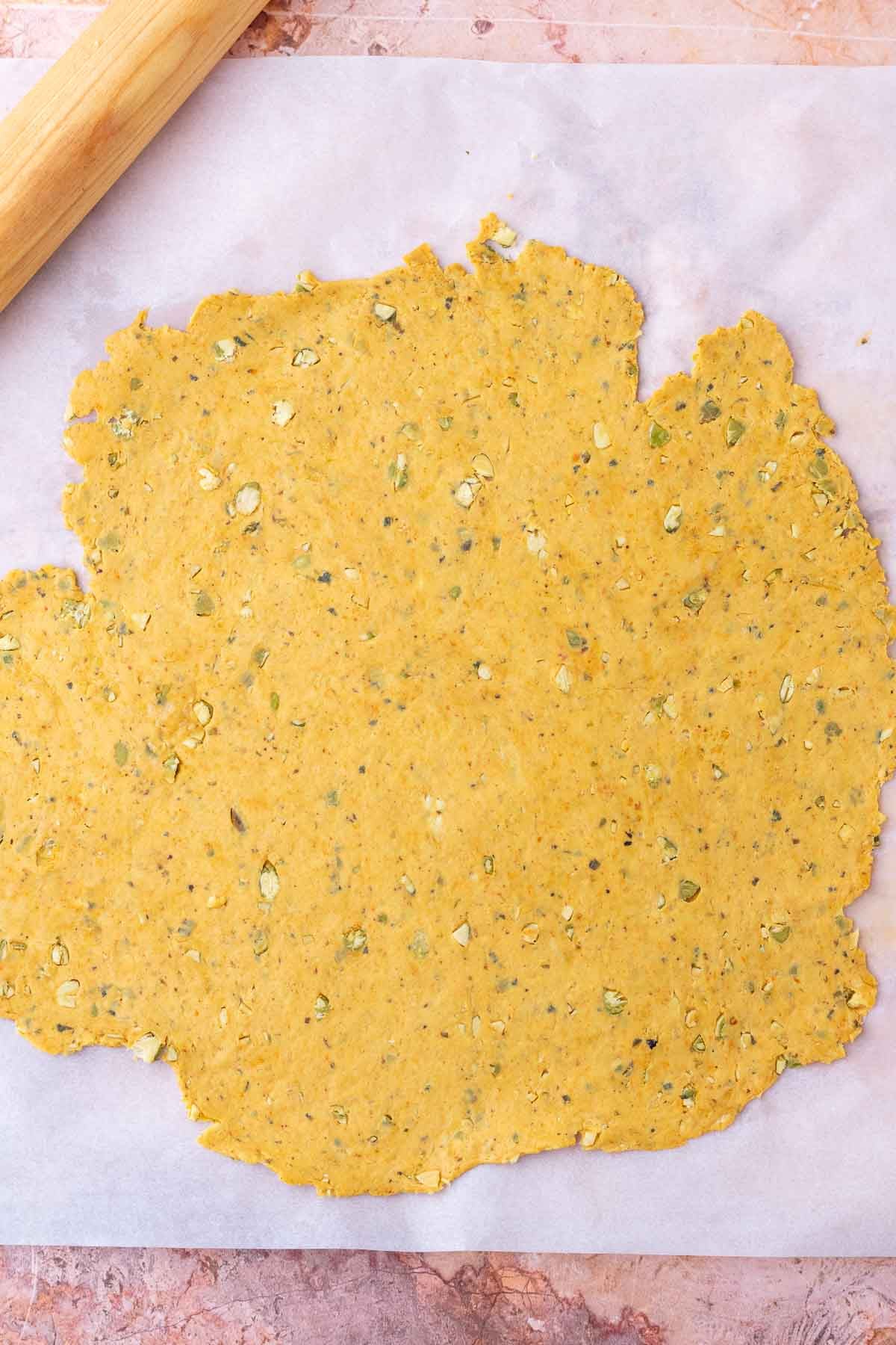 Rolled out sourdough pumpkin cracker dough on a sheet of parchment paper.