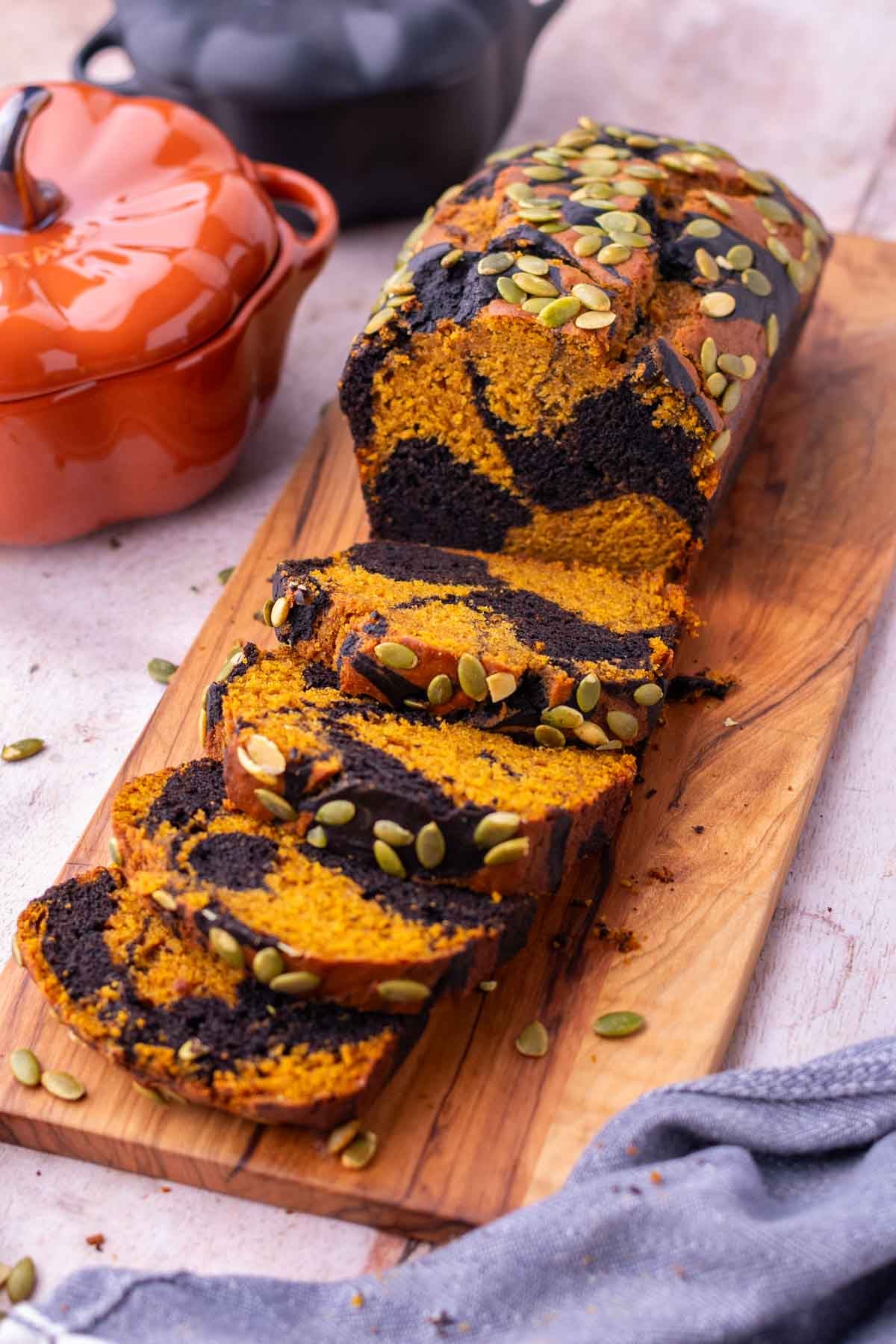 Sliced sourdough pumpkin marble bread on a cutting board with pumpkins in the background.